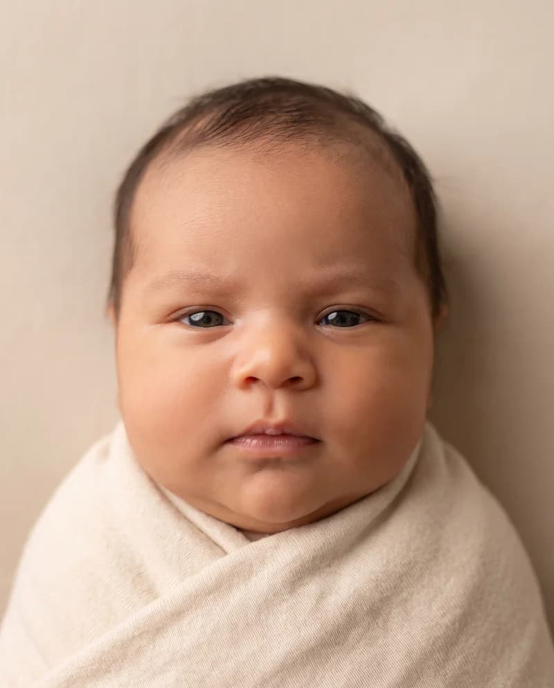 AI-created baby portrait with short brown hair and open eyes, wrapped in a cream blanket