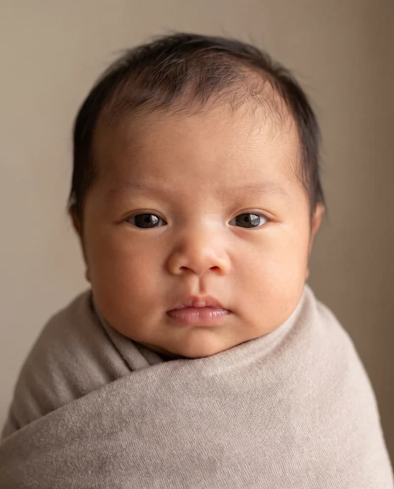 AI-created baby portrait with dark hair and open eyes, wrapped in a taupe blanket
