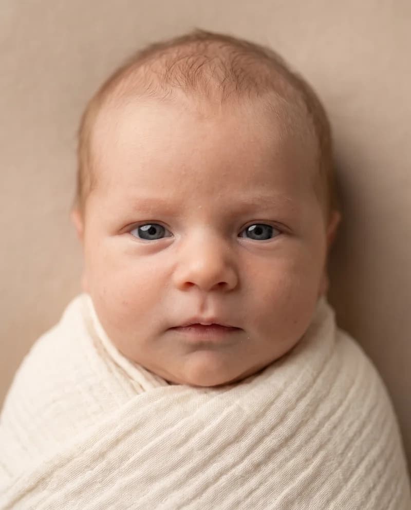 AI-created baby portrait with fine light hair and open eyes, wrapped in an ivory blanket
